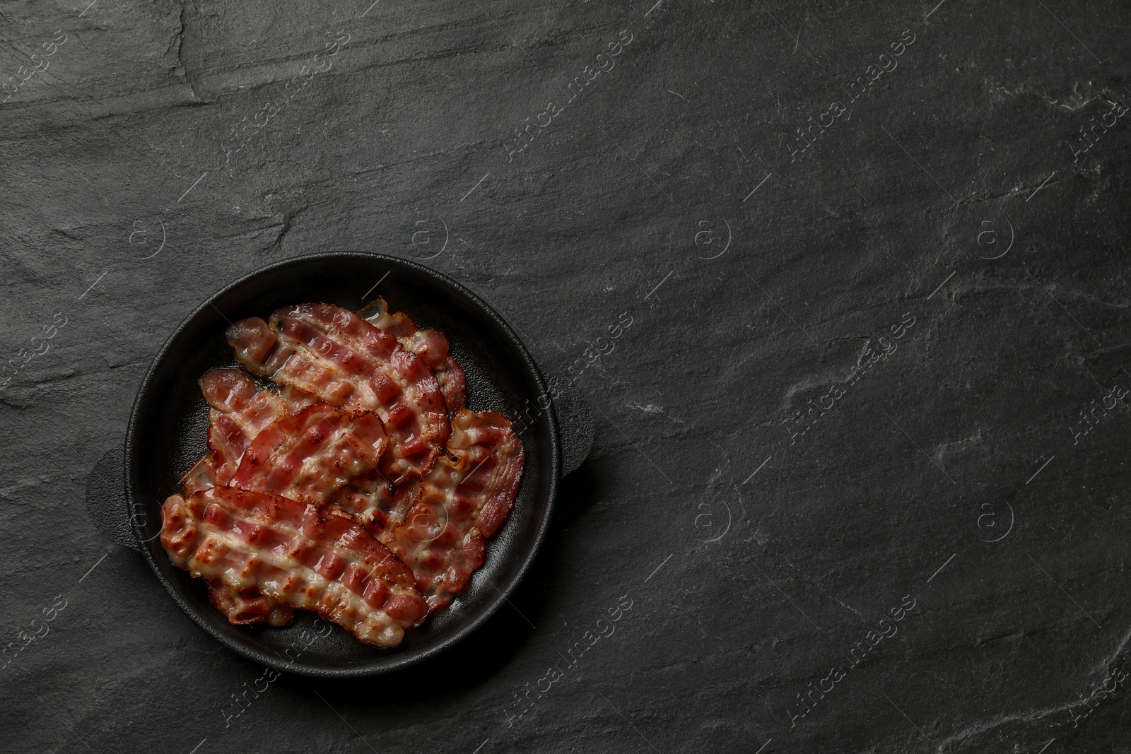 Photo of Fried bacon slices on dark textured table, top view. Space for text