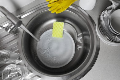 Photo of Washing plates, sponge and rubber gloves in kitchen sink, above view