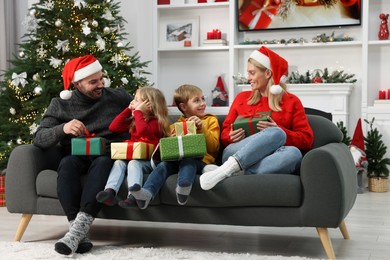 Photo of Happy family in Santa hats with Christmas gifts on sofa at home