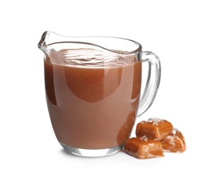 Jug of tasty caramel sauce and candies isolated on white
