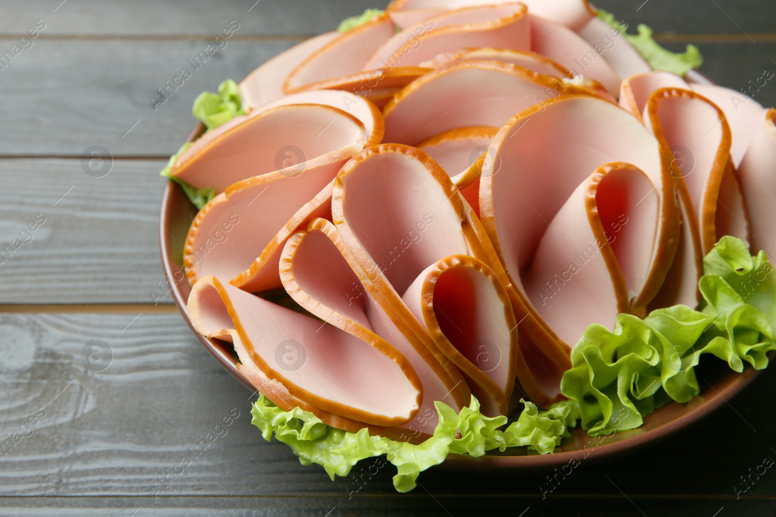 Photo of Slices of delicious boiled sausage with lettuce on dark wooden table, closeup