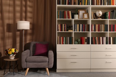 Cozy home library interior with comfortable armchair, floor lamp and collection of books on shelves