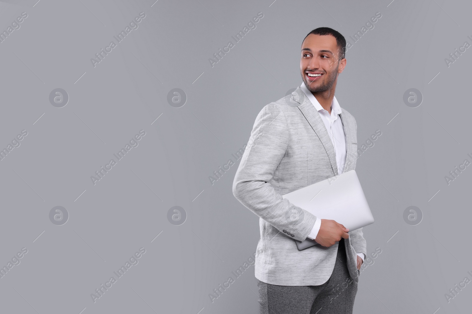 Photo of Young businessman in formal outfit with laptop on grey background. Space for text