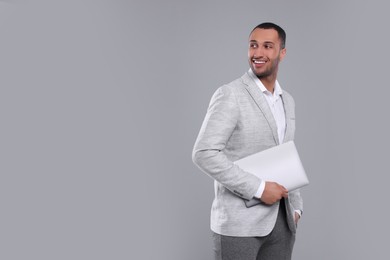 Photo of Young businessman in formal outfit with laptop on grey background. Space for text