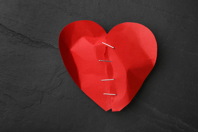 Photo of Torn paper heart with staples on black stone background, top view. Relationship problems concept