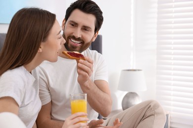 Photo of Tasty breakfast. Happy husband feeding his wife in bedroom. Space for text