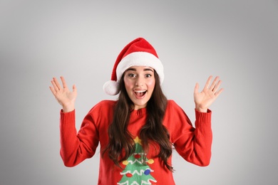 Beautiful emotional woman wearing Santa Claus hat on light grey background