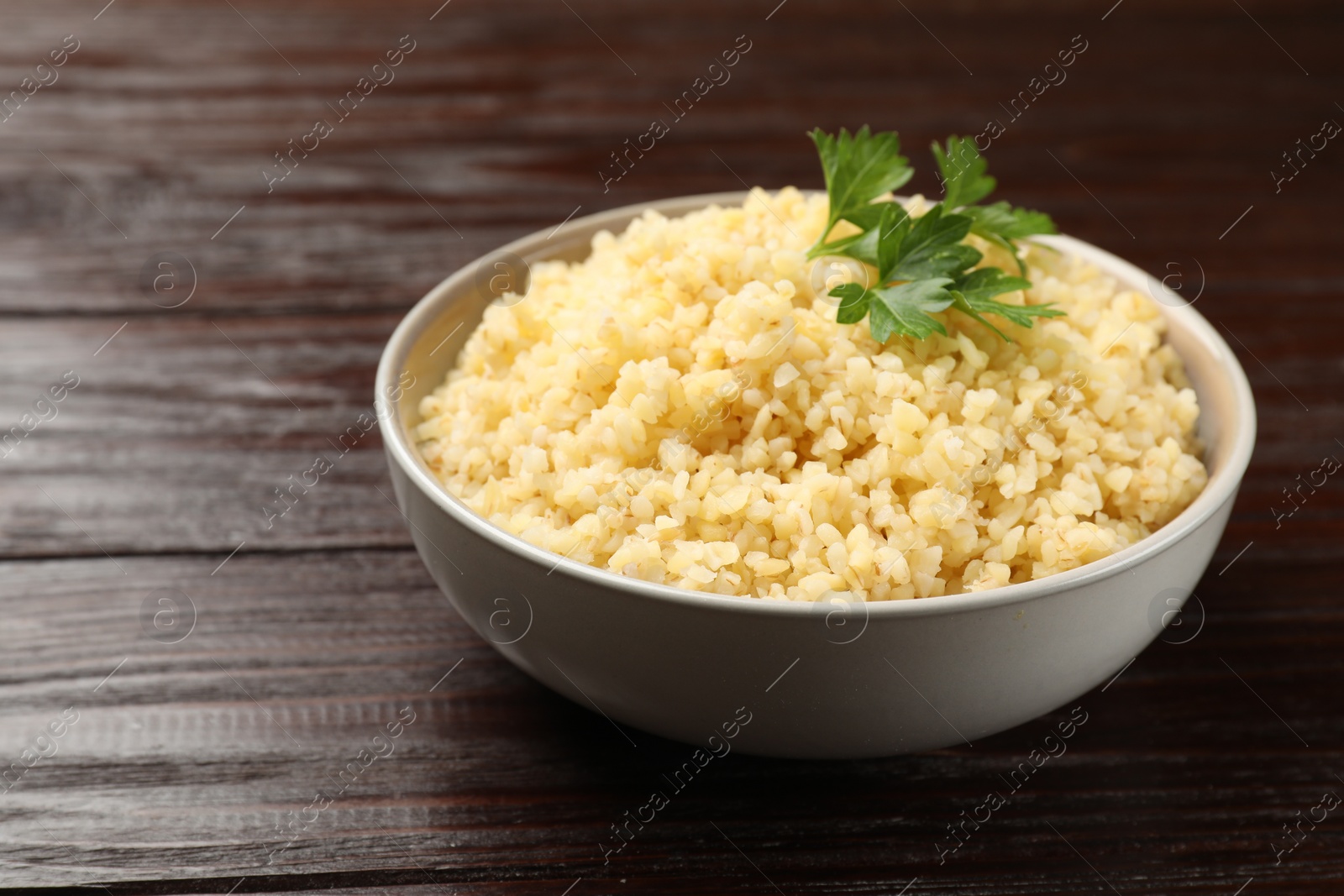 Photo of Delicious bulgur with parsley in bowl on wooden table, closeup. Space for text