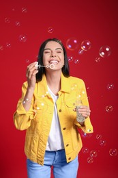 Photo of Young woman blowing soap bubbles on red background