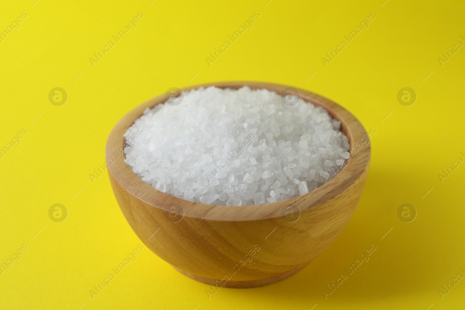 Photo of Organic white salt in bowl on yellow background