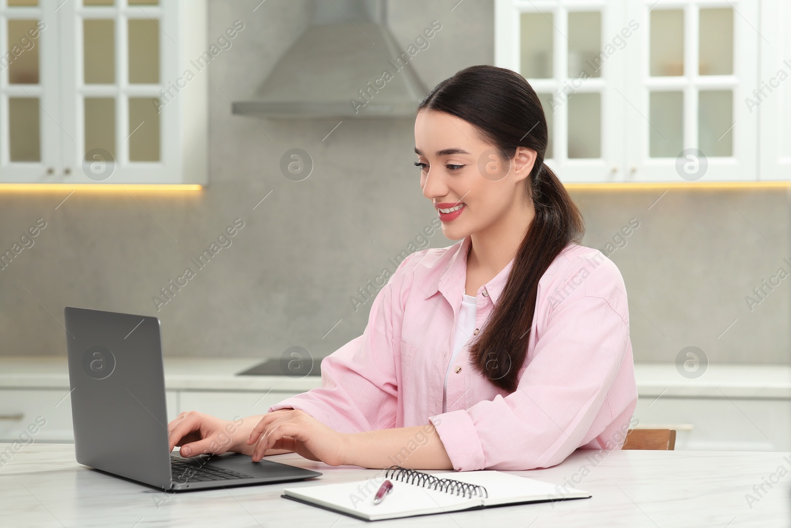 Photo of Woman using laptop at white table in kitchen