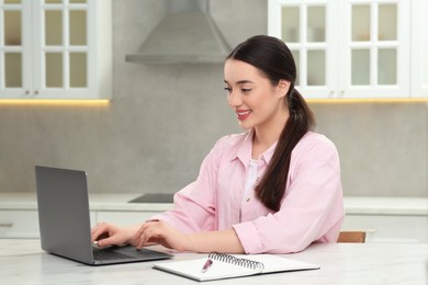 Woman using laptop at white table in kitchen