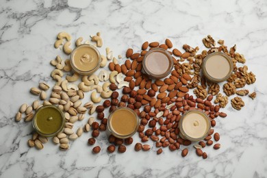 Photo of Jars with butters made of different nuts and ingredients on white marble table, flat lay