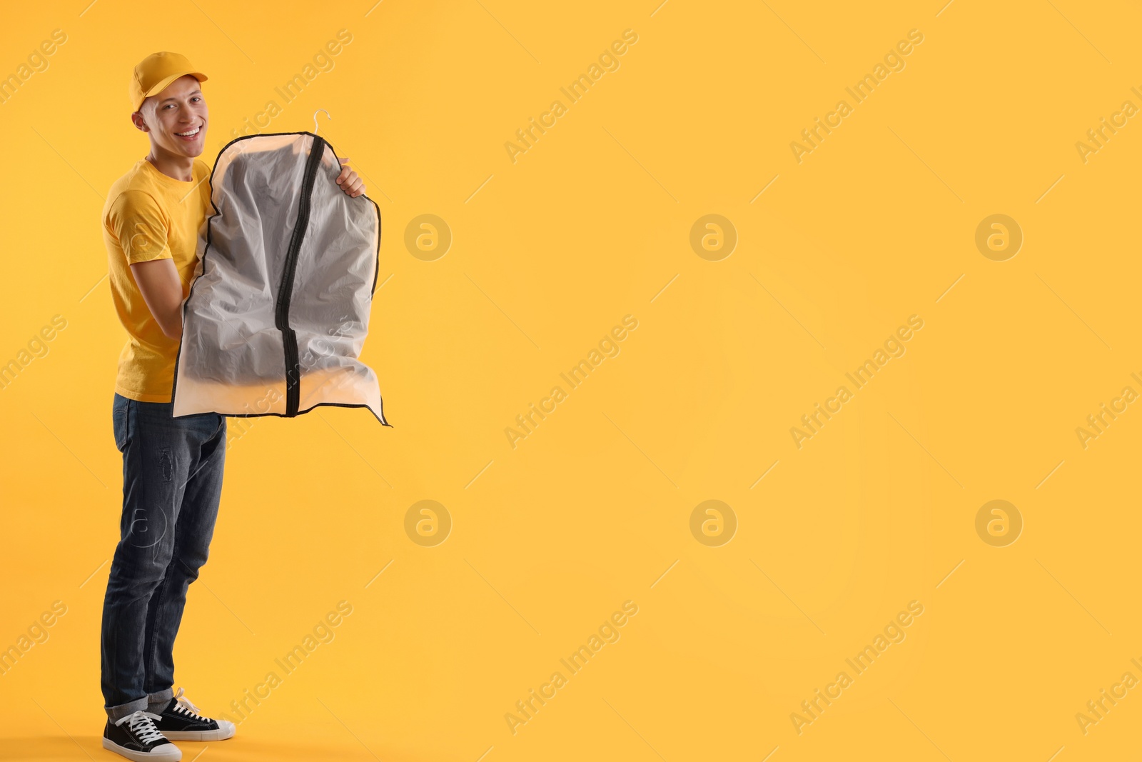 Photo of Dry-cleaning delivery. Happy courier holding garment cover with clothes on orange background, space for text