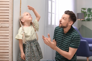 Young man helping his daughter to measure height at home