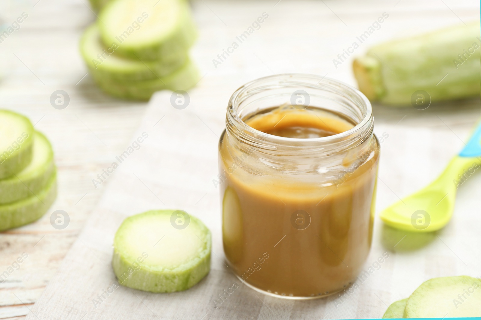 Photo of Jar with healthy baby food and zucchini on table