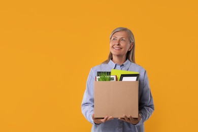 Photo of Happy unemployed senior woman with box of personal office belongings on orange background. Space for text