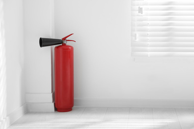 Photo of Fire extinguisher near white wall indoors. Space for text
