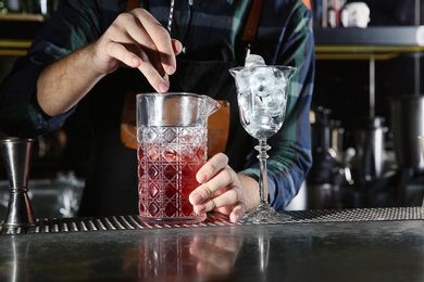 Photo of Barman mixing alcoholic cocktail at counter in night club, closeup