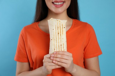 Photo of Happy young woman holding tasty shawarma on turquoise background, closeup