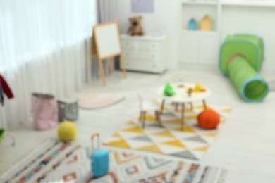 Photo of Blurred view of child`s playroom with different toys and furniture. Stylish kindergarten interior