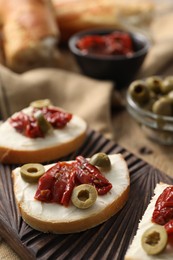 Delicious bruschettas with ricotta cheese, sun dried tomatoes and olives on table, closeup