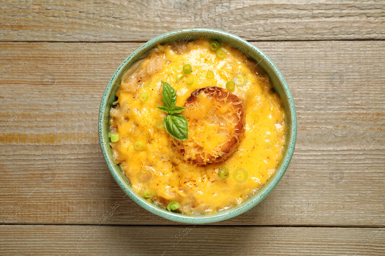 Photo of Tasty homemade French onion soup on wooden table, top view