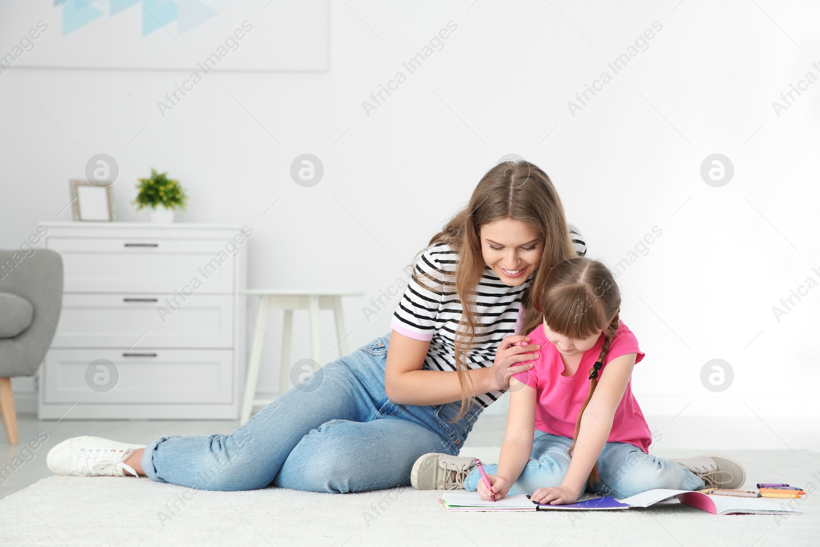 Photo of Young woman and her daughter drawing in living room. Helping to learn