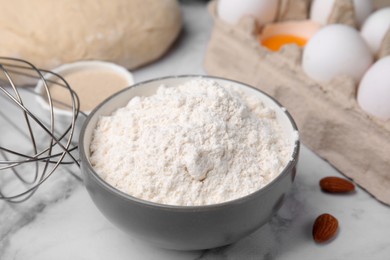 Photo of Bowl with flour on white marble table, closeup