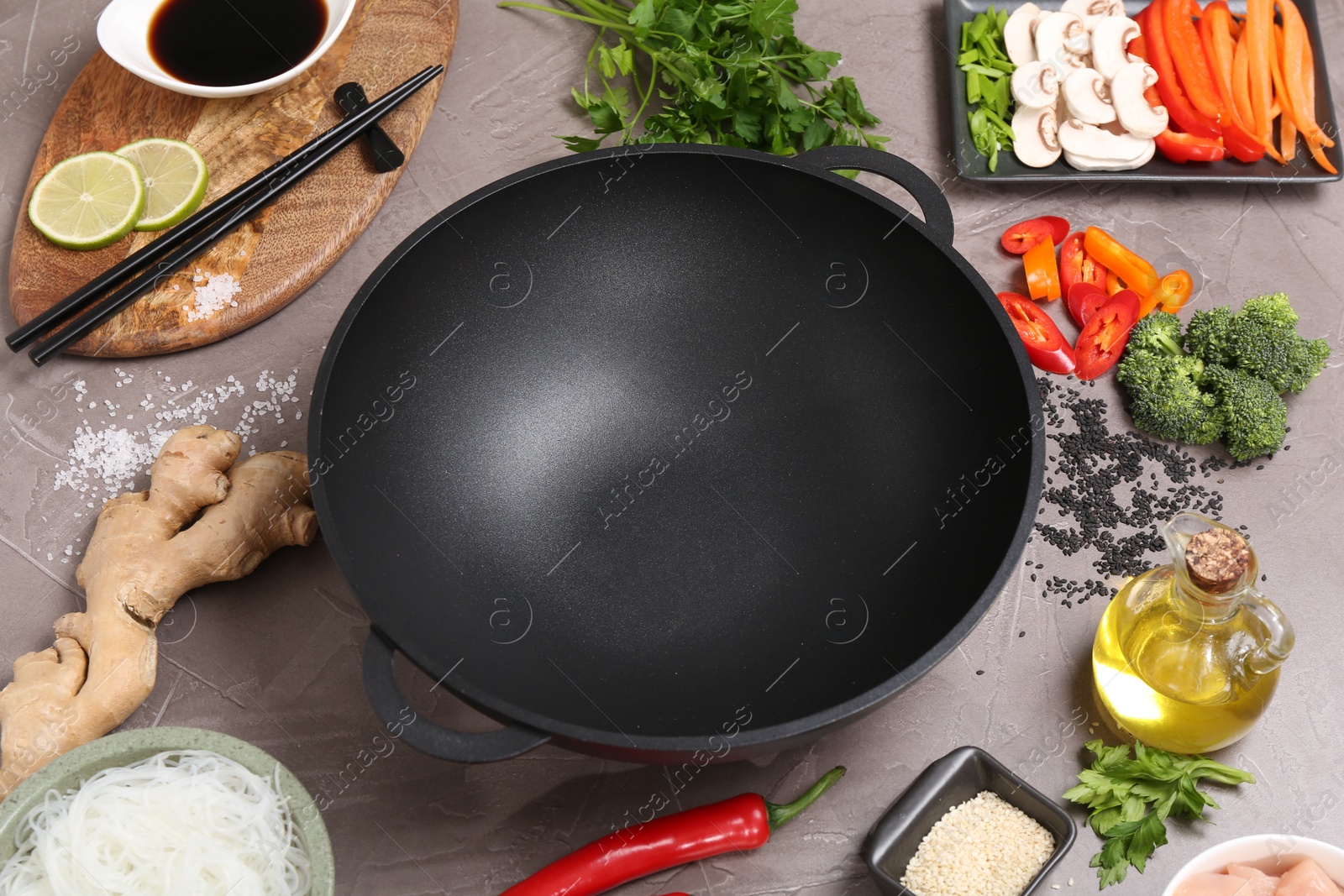 Photo of Wok, chopsticks and different products on grey textured table