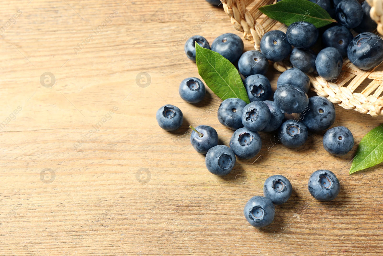 Photo of Fresh tasty blueberries with leaves on wooden table, space for text