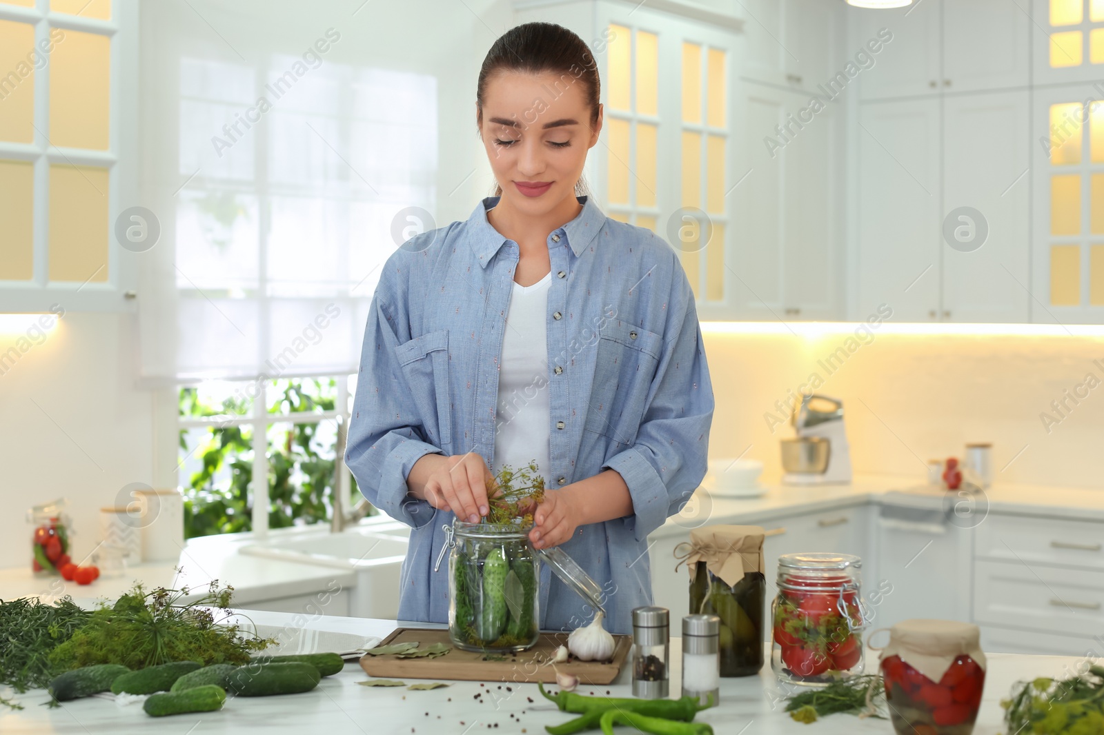Photo of Woman putting dill into pickling jar at table in kitchen