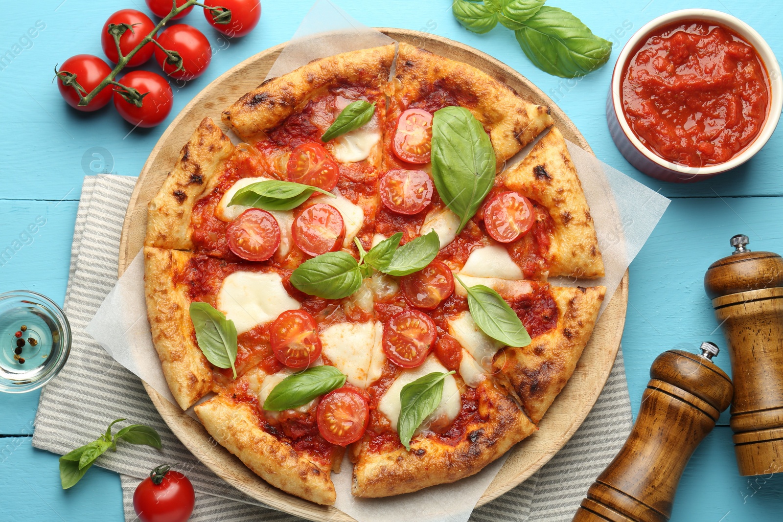 Photo of Delicious Margherita pizza and ingredients on light blue wooden table, top view