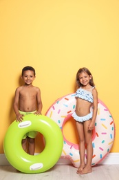 Photo of Cute little children with bright inflatable rings near color wall