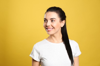 Portrait of happy young woman with beautiful black hair and charming smile on yellow background