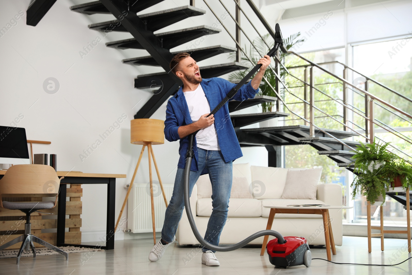 Photo of Young man having fun while vacuuming in living room