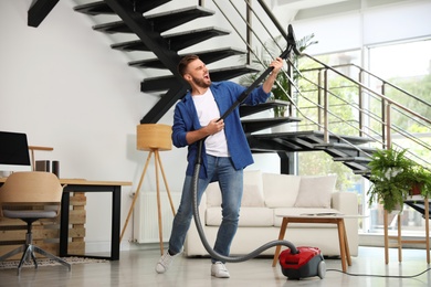 Photo of Young man having fun while vacuuming in living room