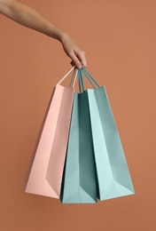 Photo of Woman holding paper shopping bags on light brown background, closeup