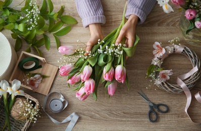 Female decorator creating beautiful bouquet at table, top view