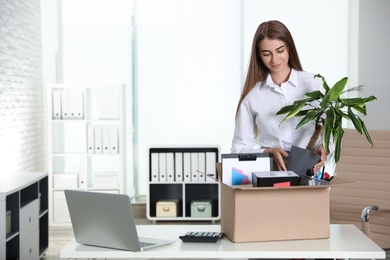 Photo of Happy young woman packing stuff in box at office