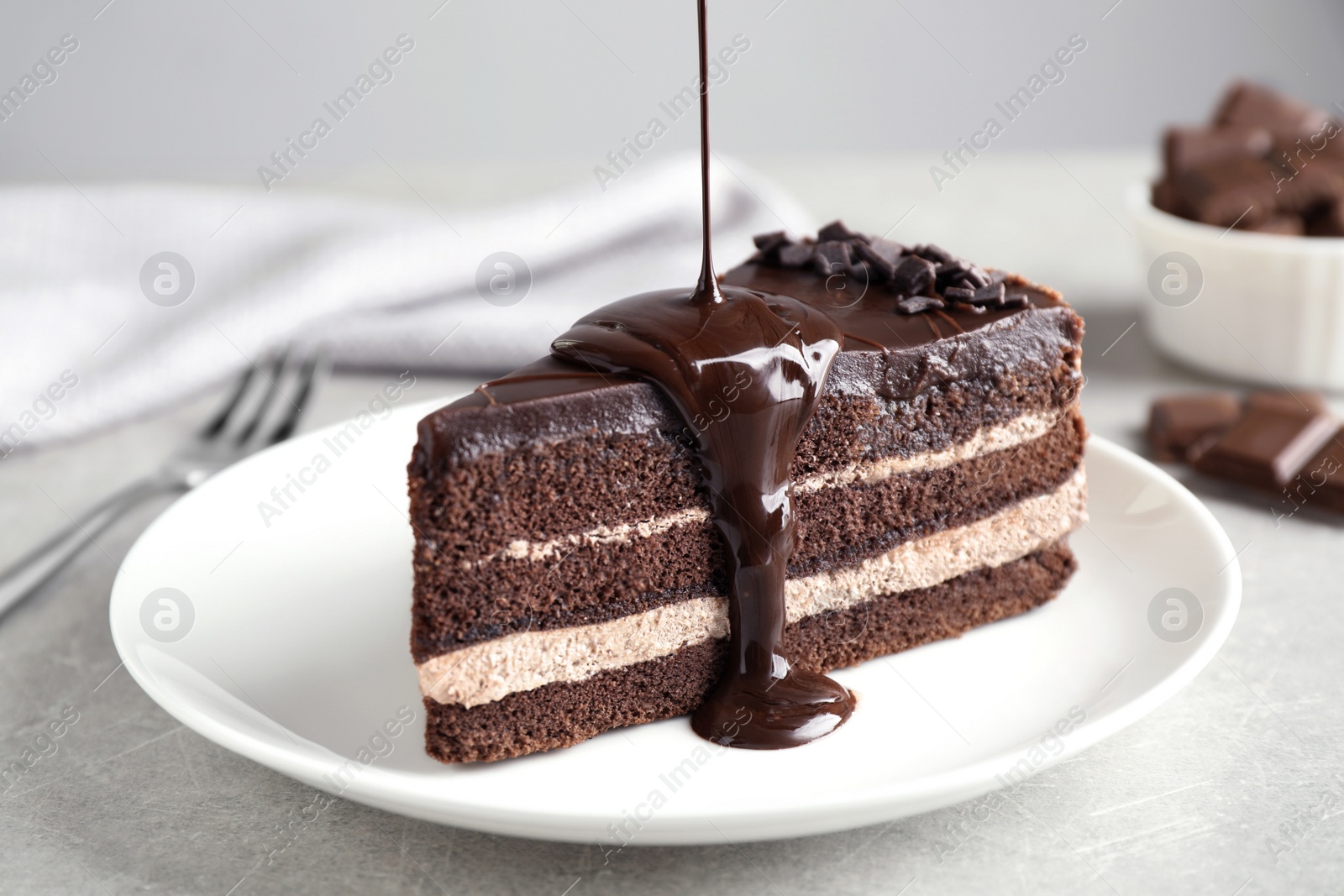 Photo of Pouring chocolate sauce onto delicious fresh cake on light table, closeup