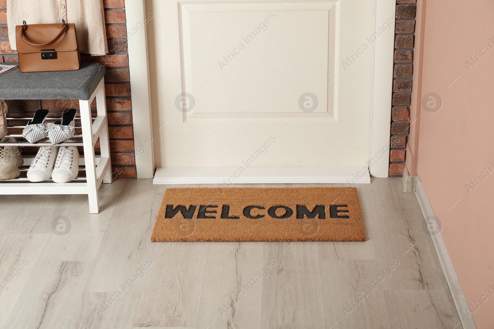 Photo of Doormat with word Welcome near shoe rack on white wooden floor in hall