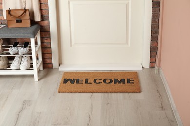Photo of Doormat with word Welcome near shoe rack on white wooden floor in hall