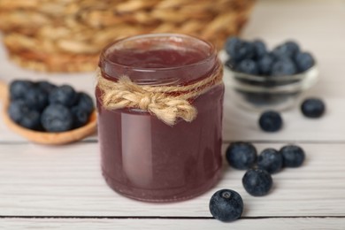 Photo of Jar of delicious blueberry jam and fresh berries on white wooden table, closeup