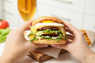 Photo of Woman holding tasty burger with fried egg over table, closeup