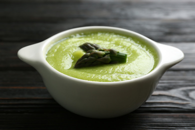 Photo of Delicious asparagus soup in bowl on black wooden table