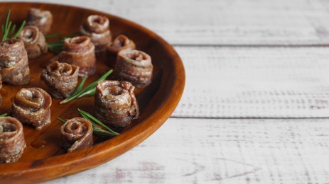 Photo of Canned anchovy fillets with rosemary on white wooden table, closeup. Space for text