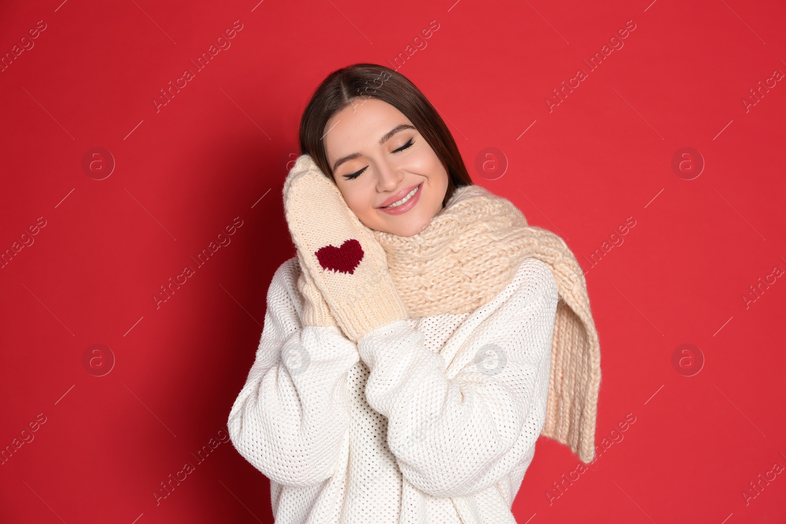 Photo of Young woman wearing warm sweater and mittens on red background. Winter season