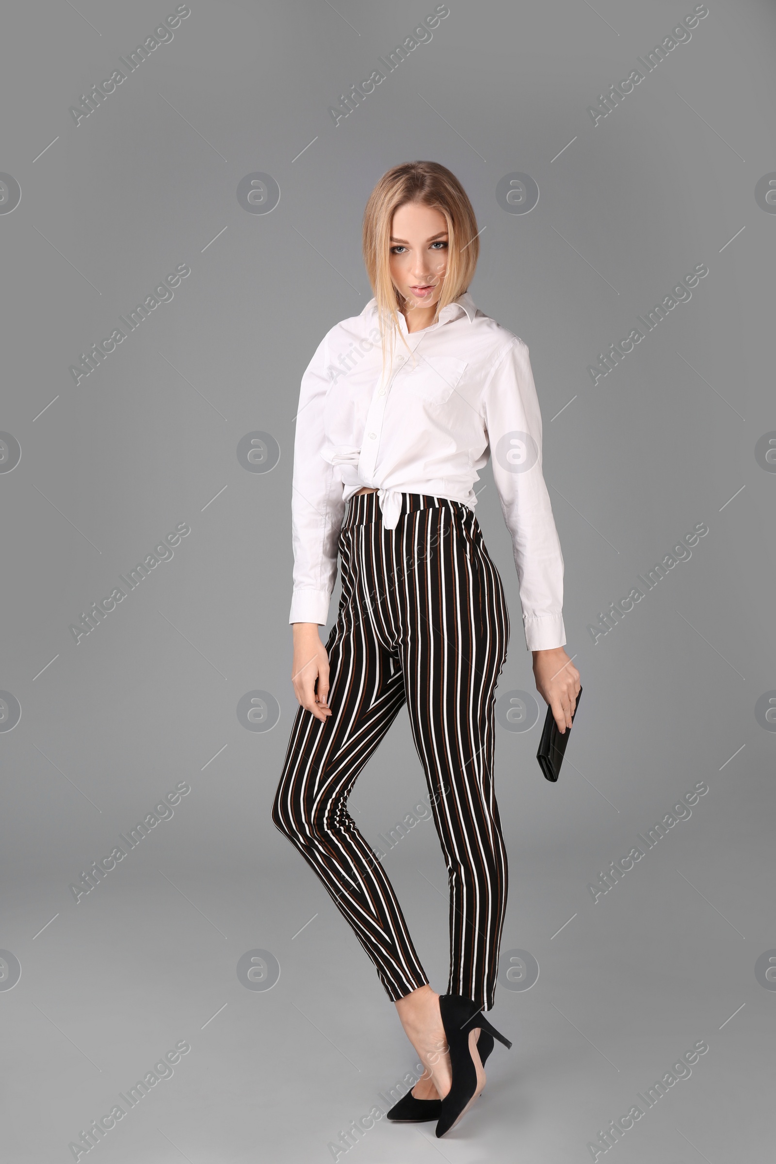 Photo of Young stylish woman in trendy shoes with bag on grey background