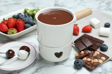 Photo of Fondue pot with chocolate, marshmallows, different berries and forks on white marble table